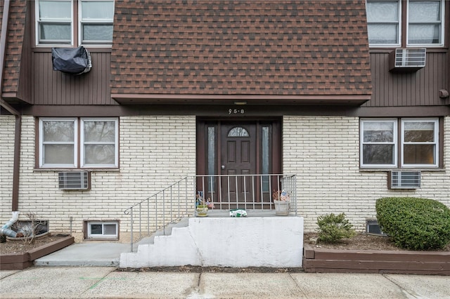 view of exterior entry featuring mansard roof, a shingled roof, and brick siding