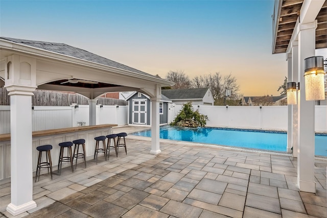 view of pool featuring a fenced in pool, outdoor dry bar, fence, an outdoor structure, and a patio area