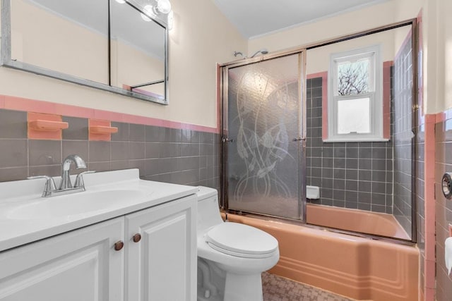 full bath featuring toilet, a wainscoted wall, enclosed tub / shower combo, vanity, and tile walls