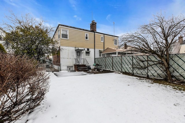 snow covered property featuring entry steps, brick siding, a chimney, and fence