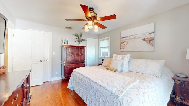 bedroom with a ceiling fan, visible vents, baseboards, and wood finished floors