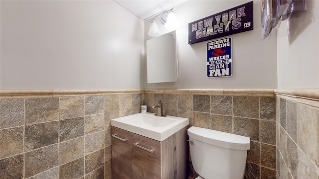 bathroom featuring wainscoting, vanity, toilet, and tile walls