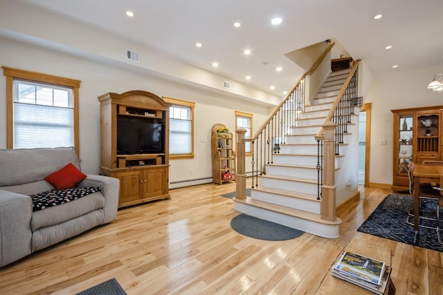 living area with light wood-type flooring, visible vents, baseboard heating, and stairs