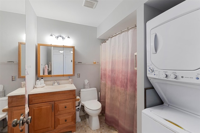 bathroom with toilet, vanity, visible vents, stacked washer / drying machine, and tile patterned floors