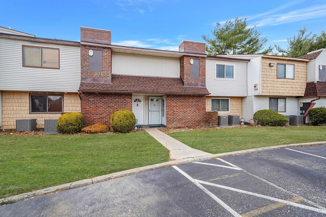 view of property with uncovered parking, a chimney, a front lawn, and brick siding