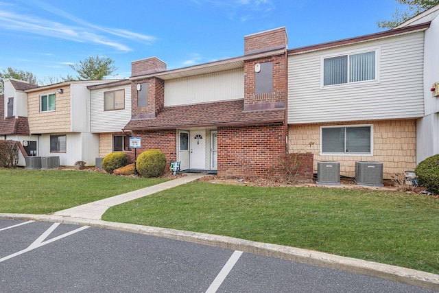 multi unit property with brick siding, a chimney, uncovered parking, central AC, and a front lawn