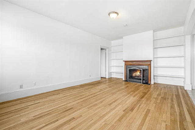 unfurnished living room with built in features, baseboards, a fireplace with flush hearth, and light wood finished floors