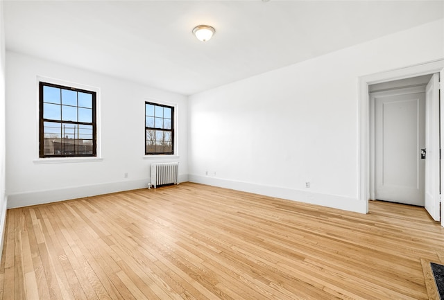 empty room featuring radiator, baseboards, and light wood-style floors