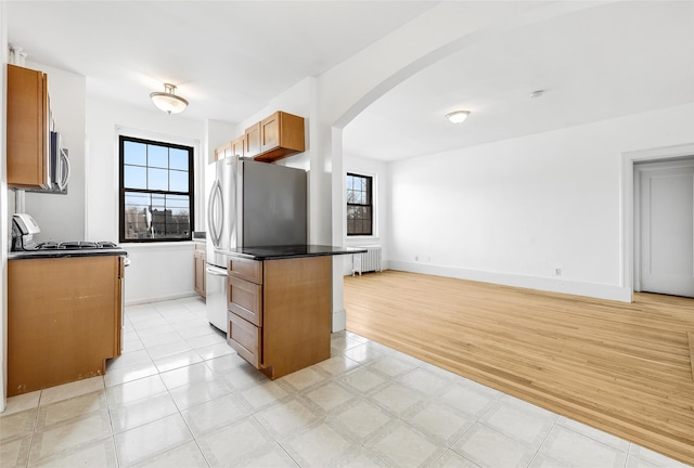 kitchen with baseboards, arched walkways, stainless steel appliances, dark countertops, and brown cabinets