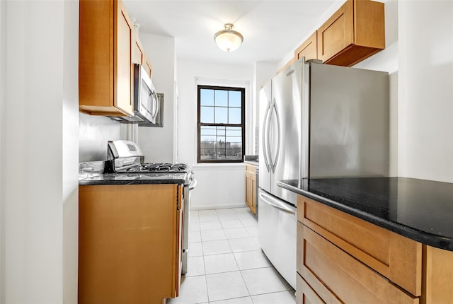 kitchen featuring baseboards, dark stone counters, light tile patterned floors, brown cabinets, and appliances with stainless steel finishes