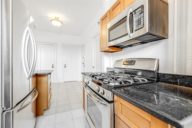 kitchen with light floors, appliances with stainless steel finishes, and dark stone counters