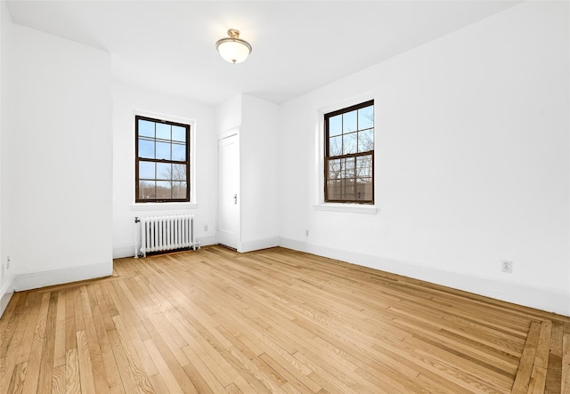 spare room featuring baseboards, a healthy amount of sunlight, radiator heating unit, and light wood finished floors