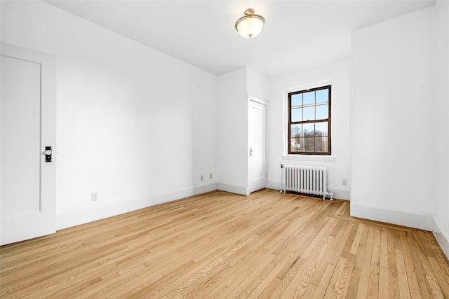 spare room featuring radiator heating unit, baseboards, and light wood finished floors