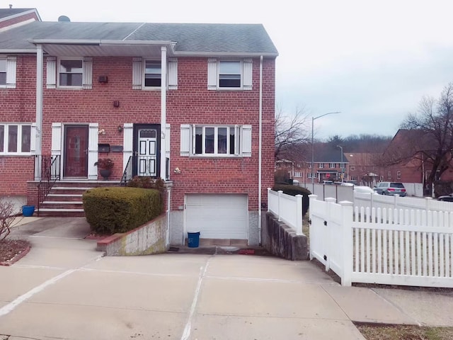 view of front of house featuring a garage, brick siding, driveway, and fence