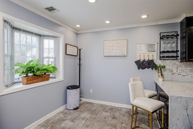 living area featuring a dry bar, baseboards, visible vents, ornamental molding, and wood finished floors