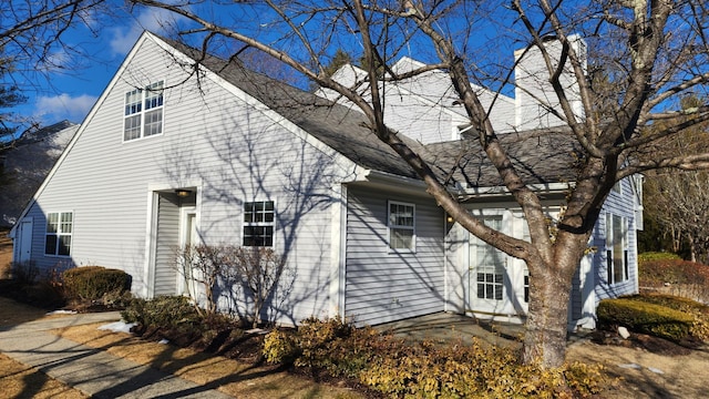 view of side of home featuring a patio and roof with shingles