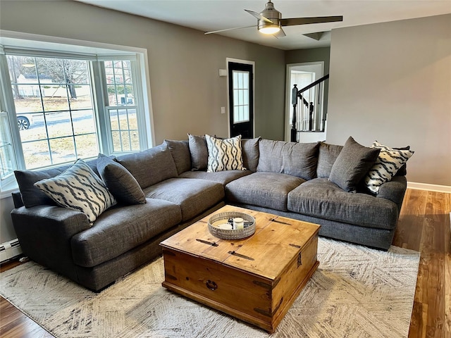 living area with a ceiling fan, baseboards, stairway, and wood finished floors