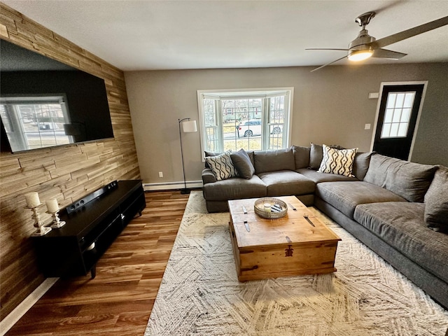 living room featuring a baseboard radiator, a ceiling fan, wood walls, wood finished floors, and baseboards