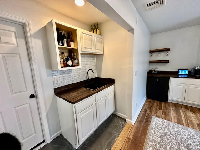 bar featuring wood finished floors, a sink, baseboards, visible vents, and decorative backsplash