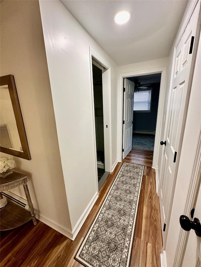 corridor featuring a baseboard radiator, baseboards, and dark wood-type flooring