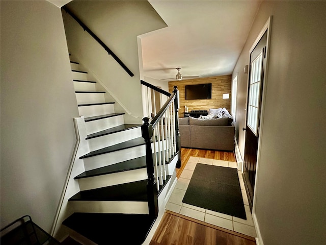 stairs featuring ceiling fan, an accent wall, wood walls, and wood finished floors