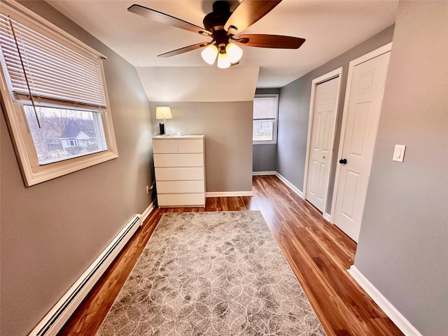 unfurnished bedroom with a baseboard heating unit, a ceiling fan, baseboards, and wood finished floors