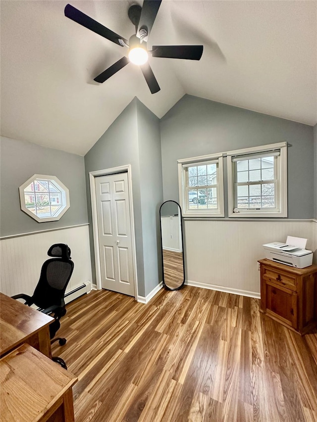 office space featuring lofted ceiling, a baseboard radiator, light wood-style flooring, a wainscoted wall, and a ceiling fan