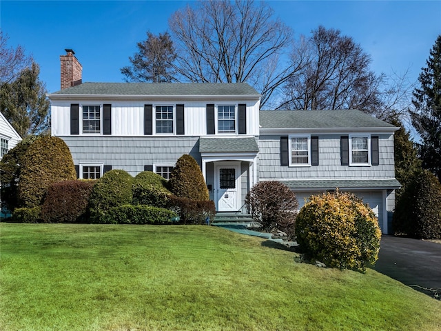 view of front of house with an attached garage, driveway, roof with shingles, a chimney, and a front yard