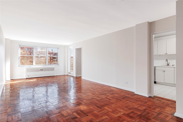 unfurnished living room featuring baseboards, a sink, and radiator heating unit