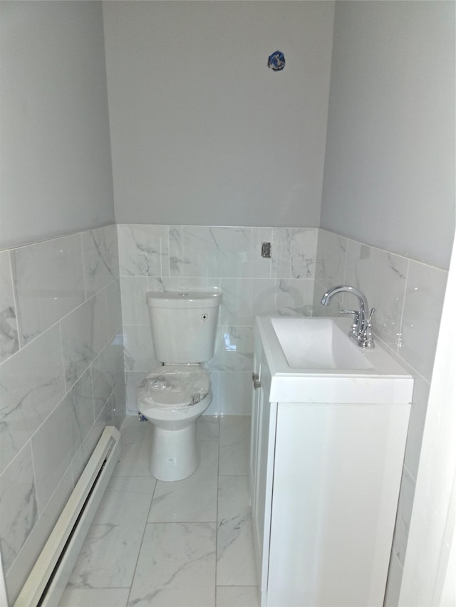 half bathroom with toilet, marble finish floor, a sink, tile walls, and baseboard heating