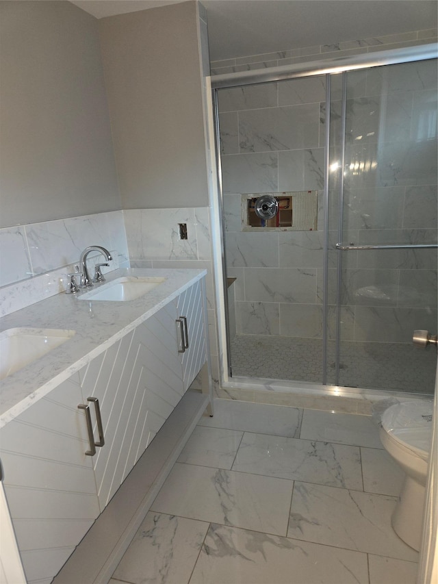 full bathroom with toilet, double vanity, a stall shower, marble finish floor, and a sink