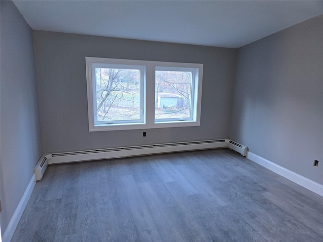 spare room featuring a baseboard radiator, baseboards, and wood finished floors