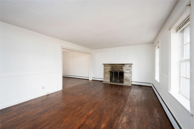 unfurnished living room with a baseboard heating unit, a stone fireplace, baseboard heating, and dark wood finished floors