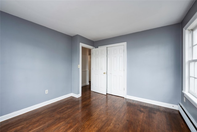 unfurnished bedroom featuring a baseboard heating unit, a closet, wood finished floors, and baseboards