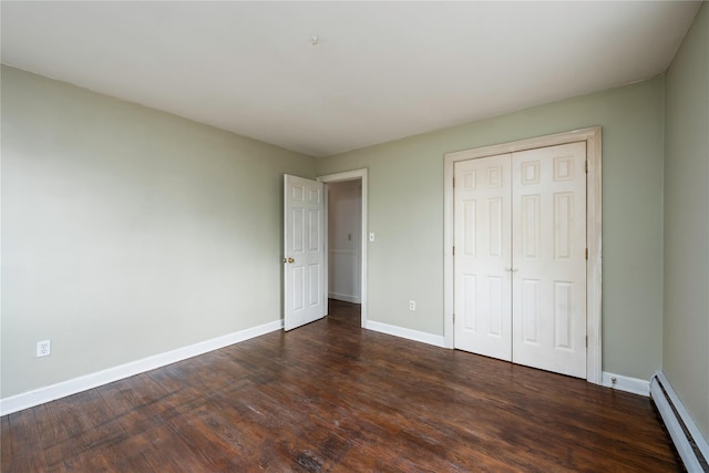 unfurnished bedroom with a closet, baseboard heating, dark wood finished floors, and baseboards