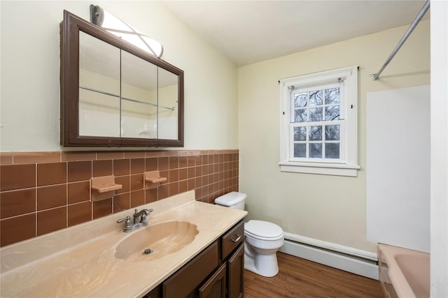 bathroom with toilet, a bathing tub, vanity, a baseboard heating unit, and tile walls