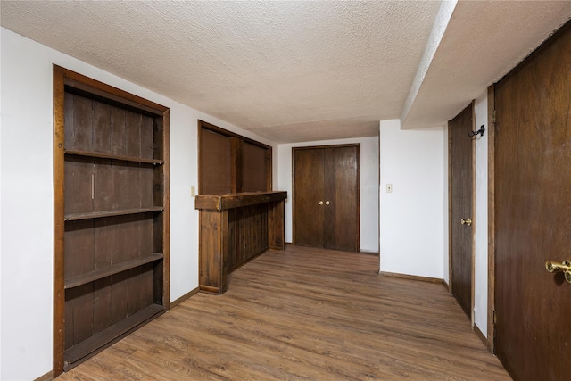 hallway with built in shelves, a textured ceiling, baseboards, and wood finished floors