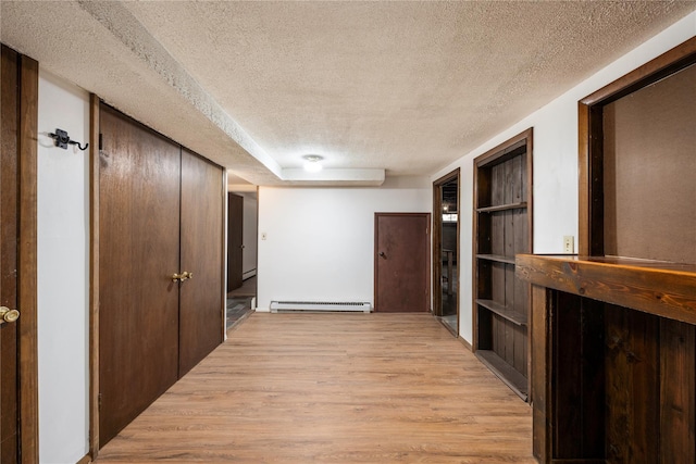 corridor with a baseboard heating unit, a textured ceiling, and light wood-style floors