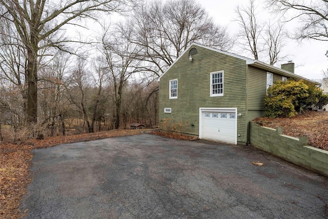 view of side of property featuring driveway, an attached garage, and a chimney