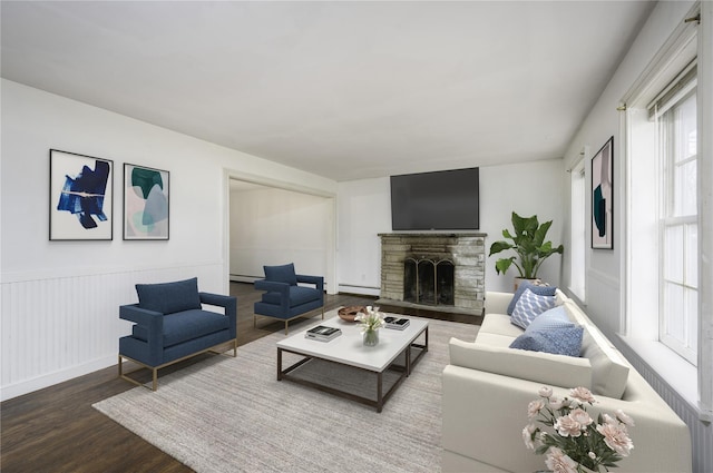 living room with baseboard heating, a fireplace, a wainscoted wall, and wood finished floors