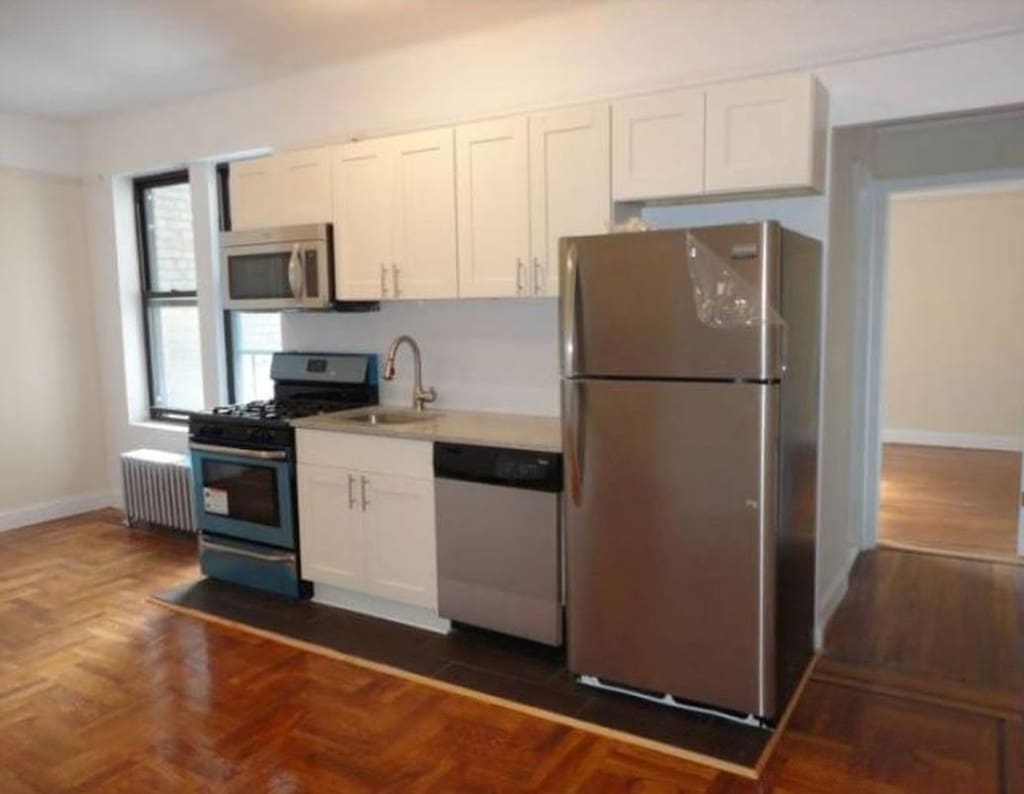 kitchen with appliances with stainless steel finishes, white cabinets, a sink, and radiator heating unit