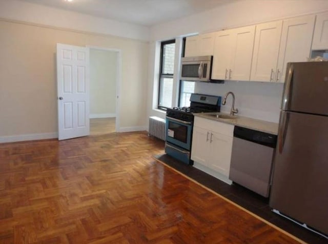 kitchen featuring white cabinets, radiator heating unit, appliances with stainless steel finishes, light countertops, and a sink