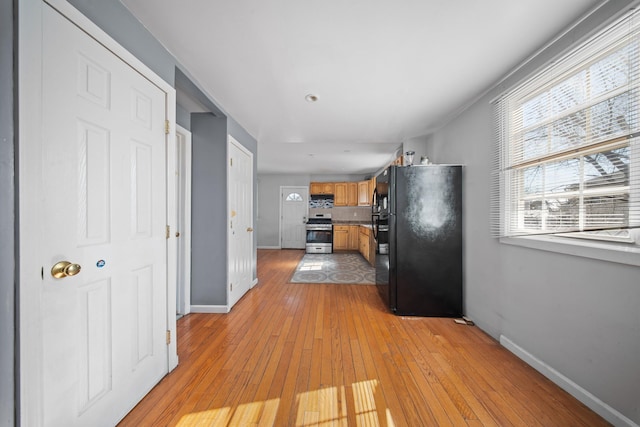 kitchen featuring baseboards, stainless steel range with gas stovetop, freestanding refrigerator, and light wood-style floors