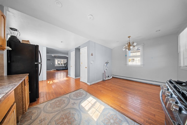 kitchen with a baseboard radiator, an inviting chandelier, brown cabinetry, freestanding refrigerator, and stainless steel range with gas stovetop