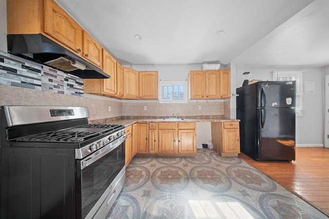 kitchen with gas range, light countertops, freestanding refrigerator, and under cabinet range hood