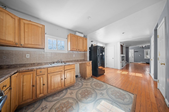 kitchen with baseboards, freestanding refrigerator, a sink, light wood-style floors, and backsplash