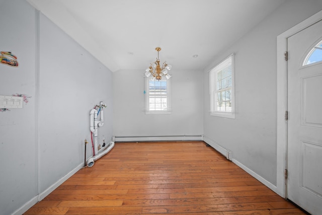 unfurnished dining area with a baseboard heating unit, a notable chandelier, light wood-style flooring, and baseboards