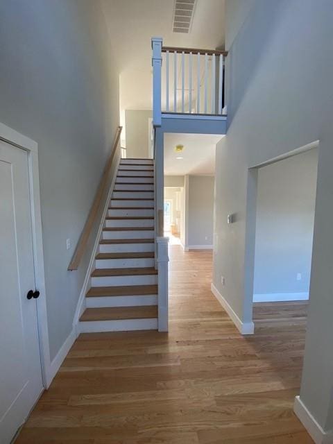 stairs with visible vents, wood finished floors, a towering ceiling, and baseboards