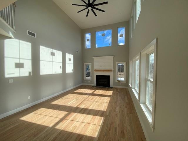 unfurnished living room featuring a fireplace with flush hearth, wood finished floors, a wealth of natural light, and baseboards