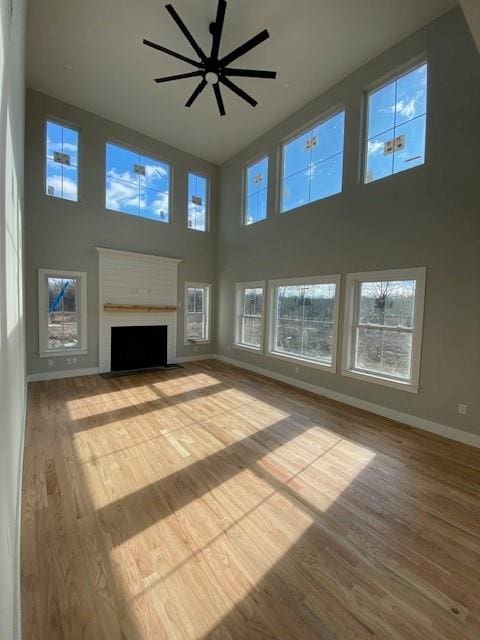 unfurnished living room with a fireplace with flush hearth, ceiling fan, wood finished floors, and baseboards